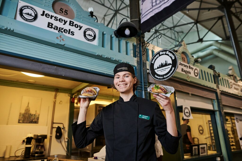 Virgile Hero hymyilee kameralle bagelit käsissään Tampereen Kauppahallissa