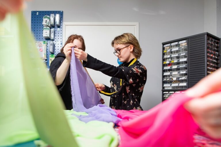 Kuvassa kaksi ompelijaopiskelijaa valitsemassa eriväsiä kankaita.