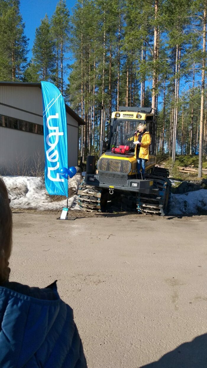 Regina Blom puhumassa mikkiin työkoneen päällä ulkona.