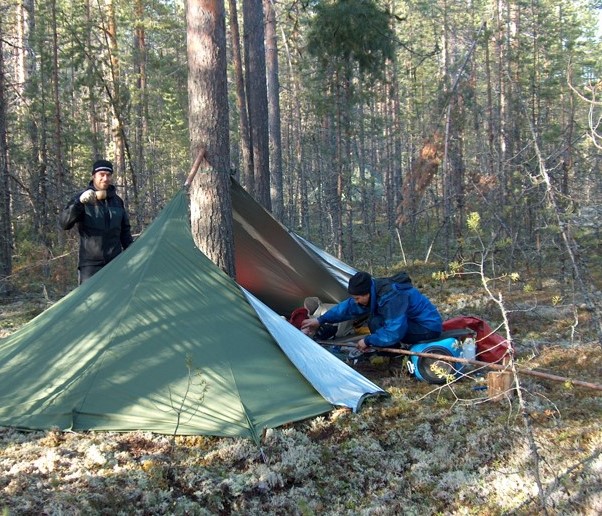 Teltta pystytetty puun ympärille ja kaksi opiskelijaa