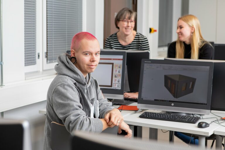 Punahiuksinen opiskelija istuu hymyillen tietokoneen äärellä.