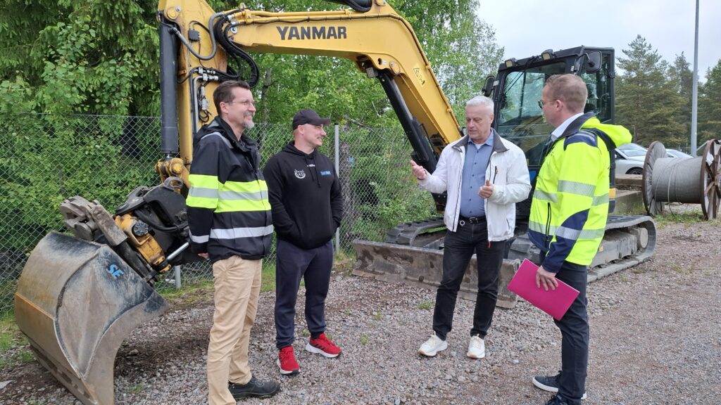 Maansiirtoajokoulutuksen vastuuhenkilöt keskustelemassa työkoneen edessä.