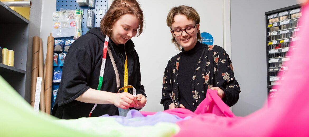 Tekstiilialan opiskelijat levittävät kankaita pöydälle.
