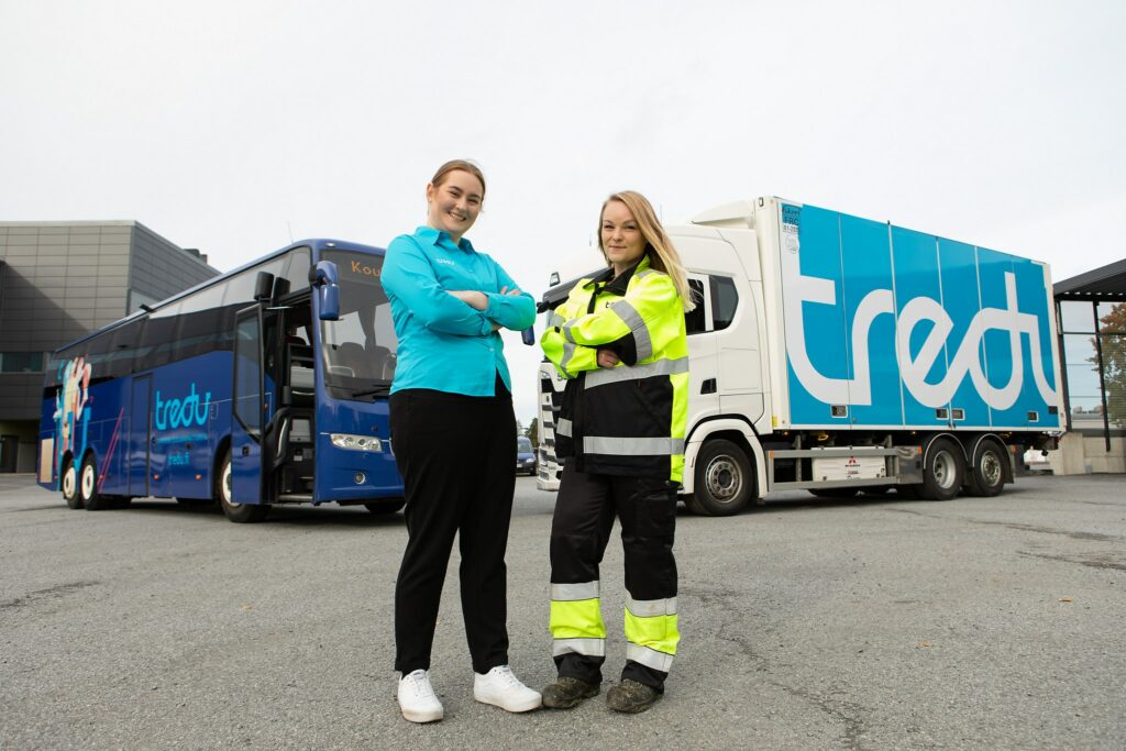 Kaksi logistiikka-alan opiskelijaa, takana Tredun bussi ja kuorma-auto.