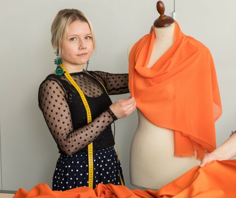 Nainen sovittaa oranssia vaatetta mallinuken päälle.