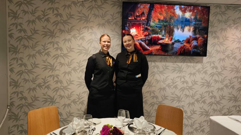 Tarjoilijaopiskelijat Oona Mäntyniemi ja Aino Ahvonen katsovat kameraan hymyillen.